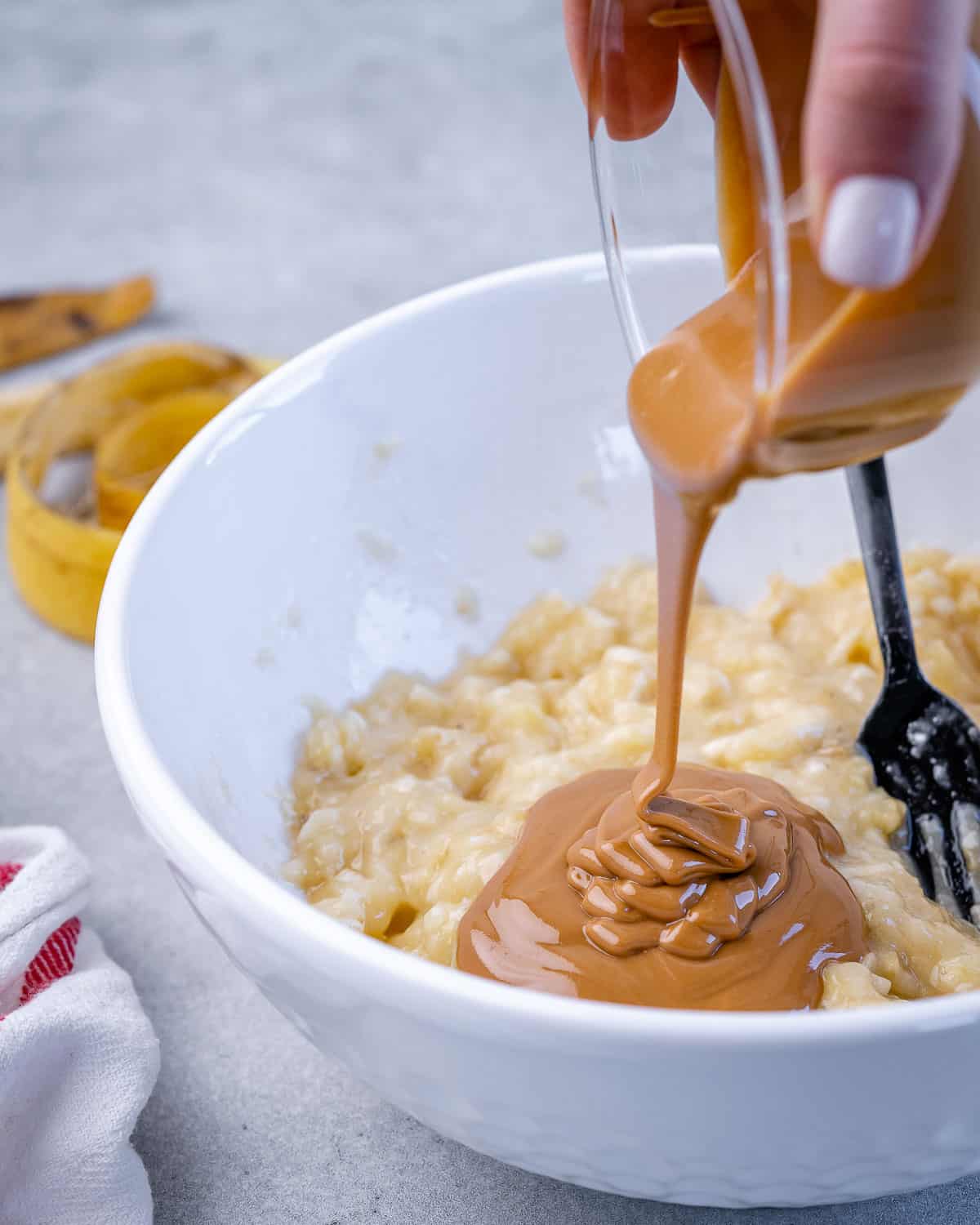 pouring peanut butter over mashed banana in white bowl