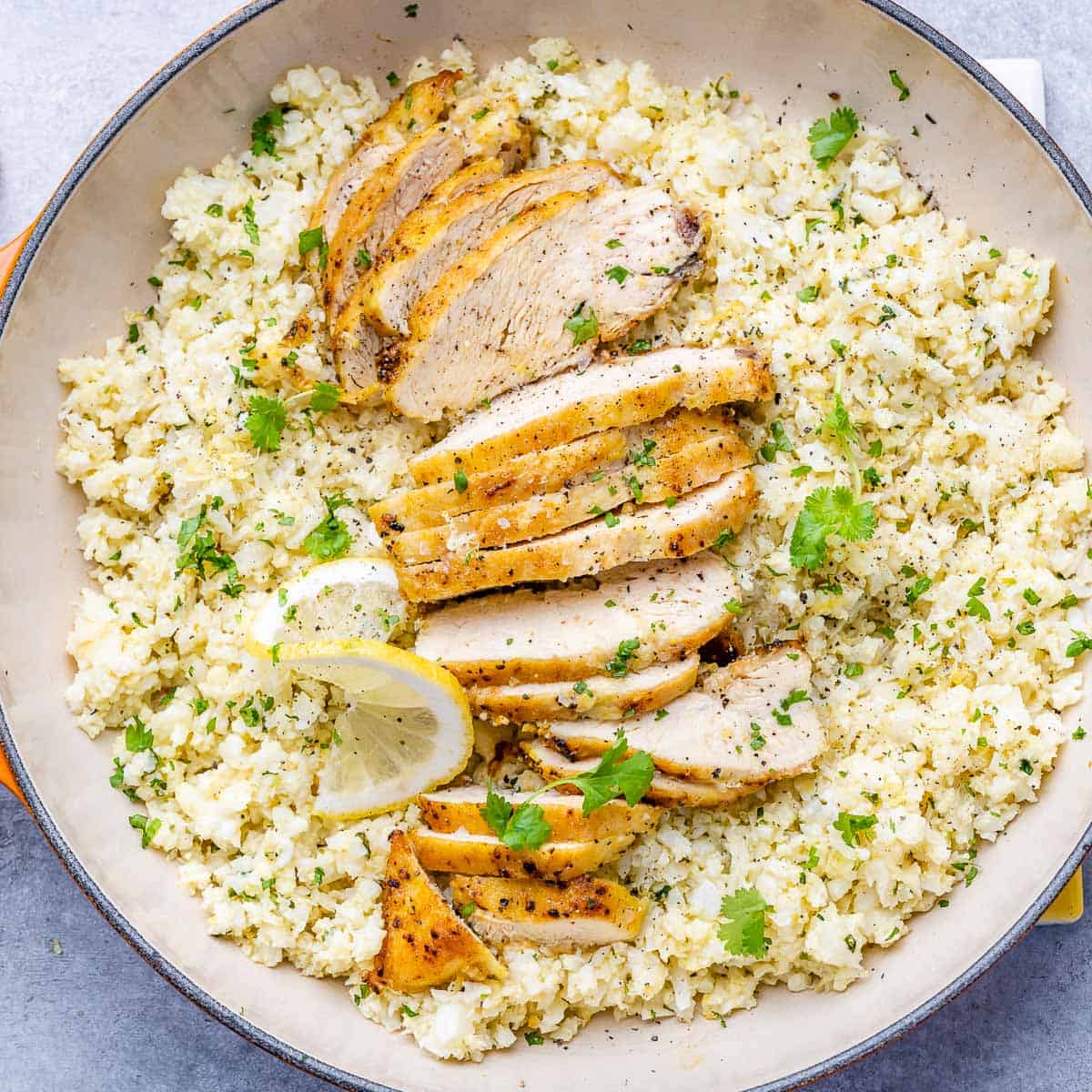 top view cauliflower rice in a skillet with sliced chicken breast