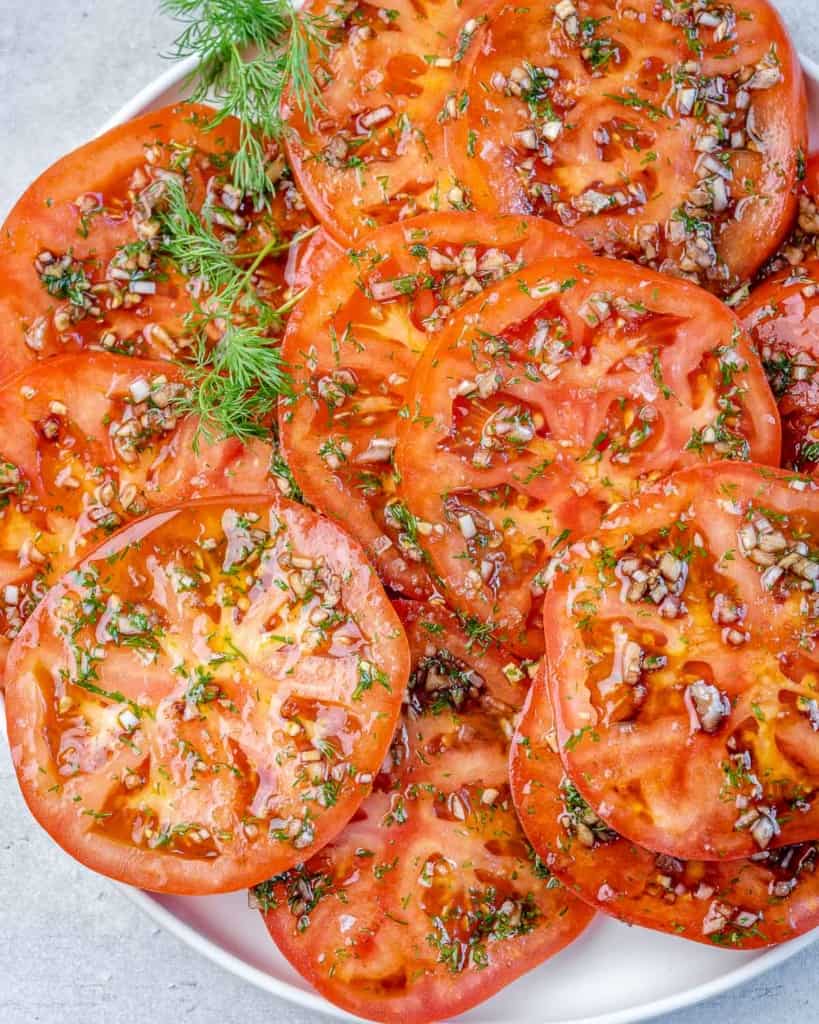 close up sliced marinated tomatoes on a white plate 