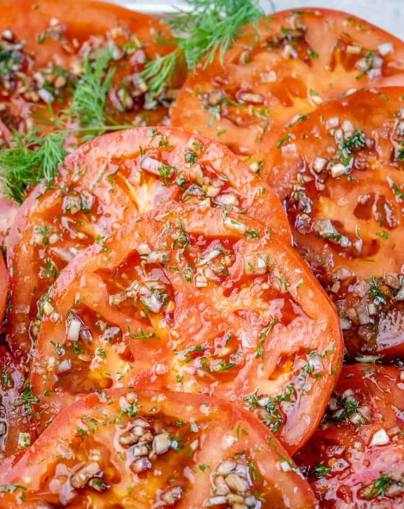 close up sliced marinated tomatoes topped with herbs 