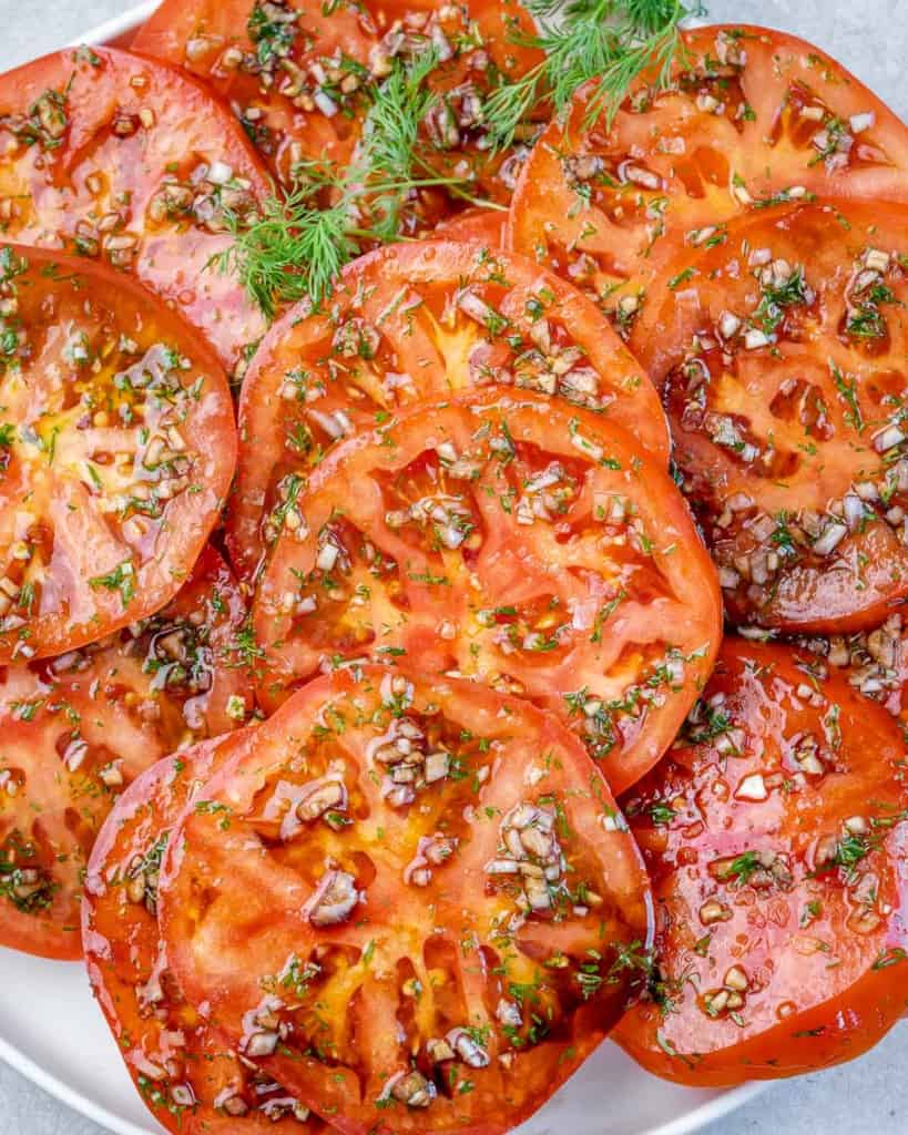 side view of sliced marinated tomatoes on a white plate 
