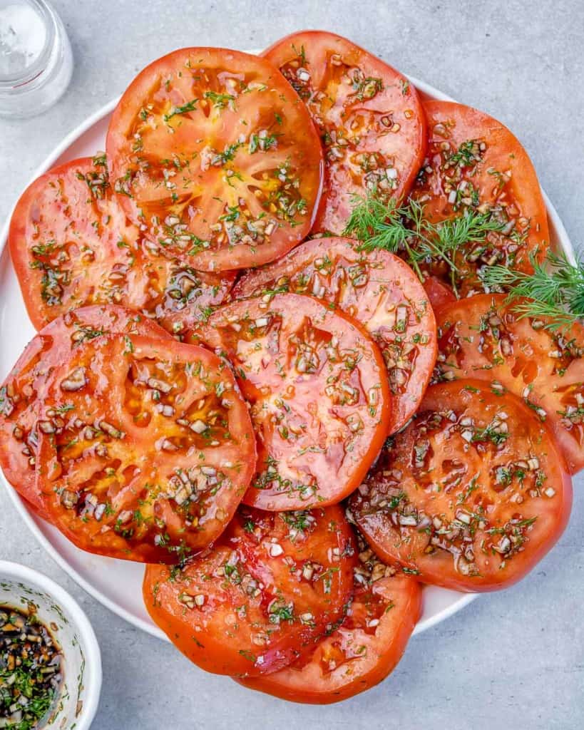 top view sliced tomatoes marinated in herbs on a white plate 