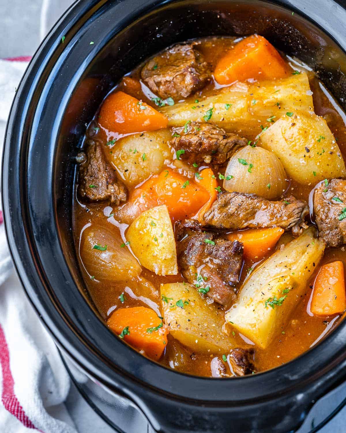 top view of potatoes, onions, carrots, beef tips, and broth in Crockpot 