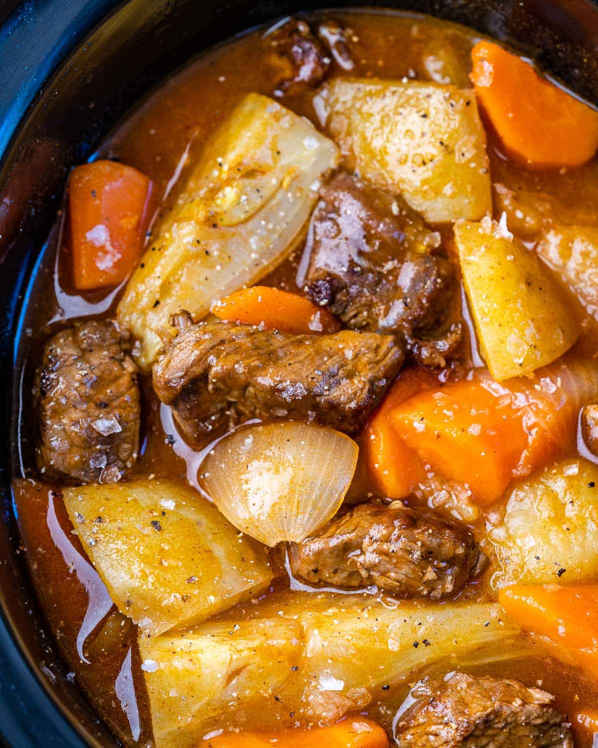 very close image of onions, carrots, beef, and potatoes in Crockpot with broth and seasoning