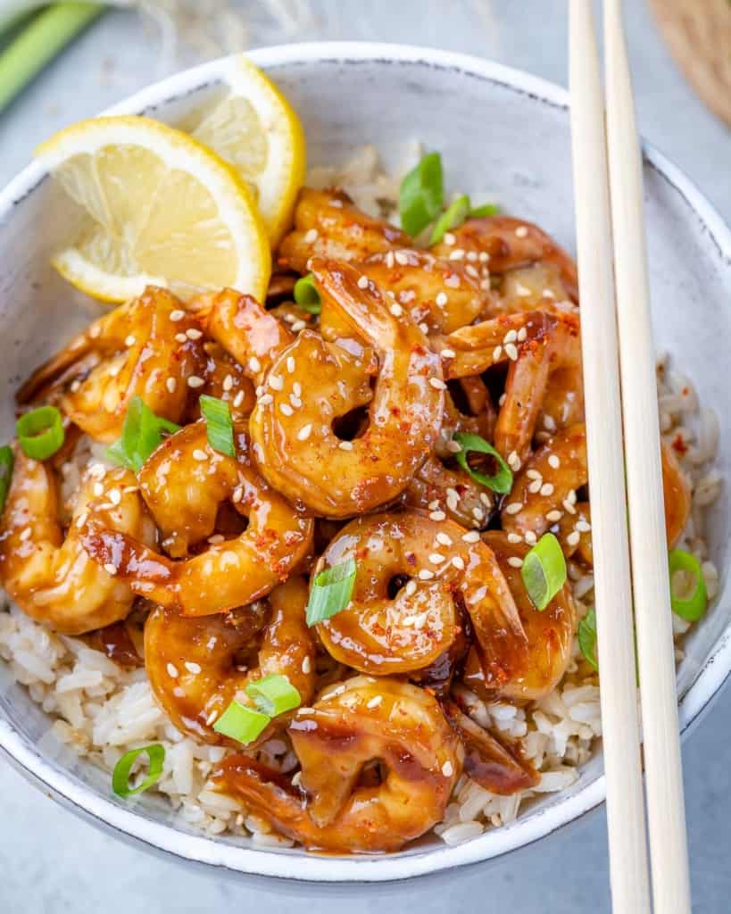top view of teriyaki shrimp over rice in a white bowl with two side of chop sticks 