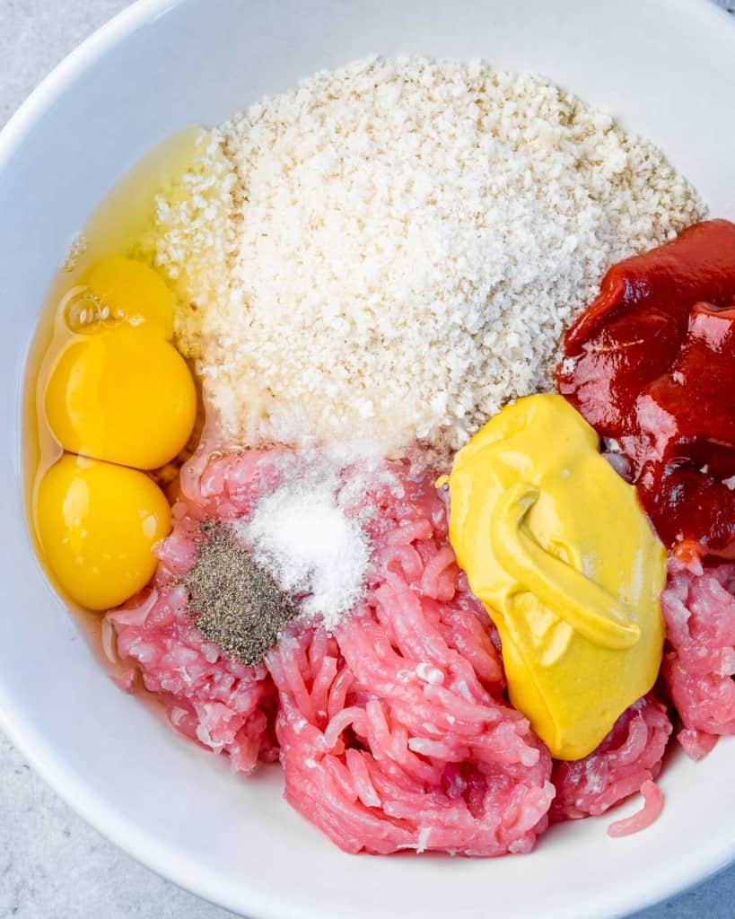 ingredients of meatload added to bowl- eggs, ground turkey, salt and pepper, mustard, ketchup, and breadcrumbs