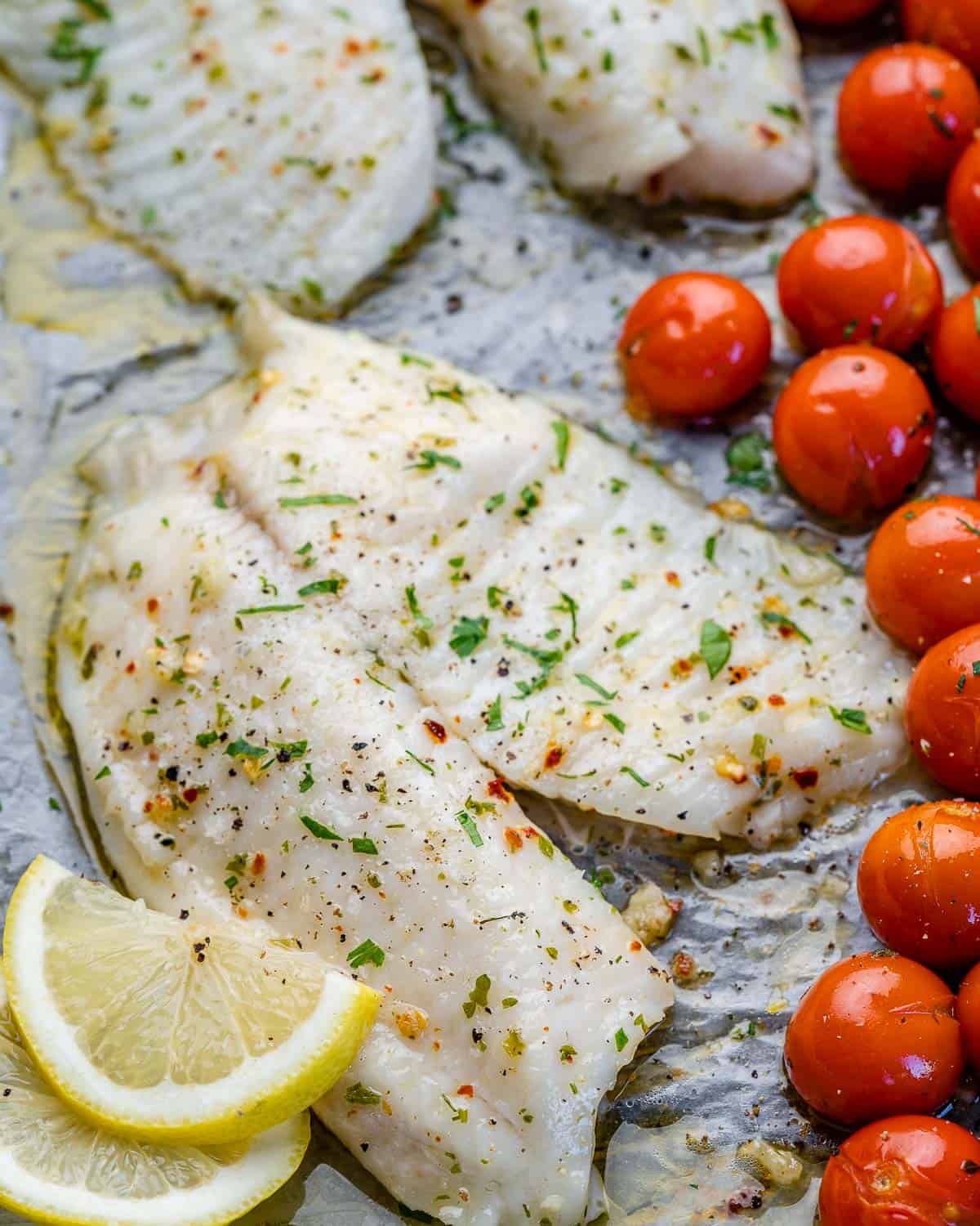 two tilapia fish fillets with parsley, lemon, and tomatoes