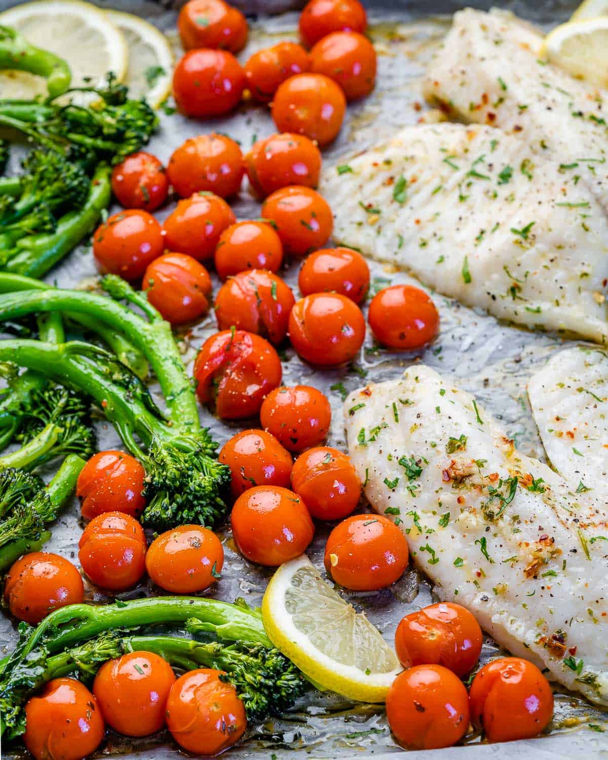 cherry tomatoes on baking sheet with tilapia, lemon, and broccolini