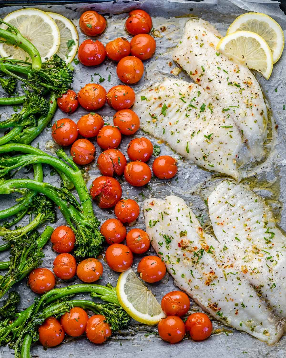 top view of fish fillets on baking sheet with tomatoes and broccolini