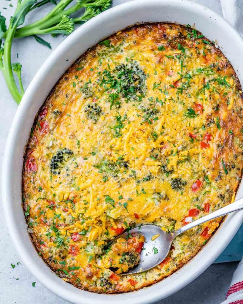 top view breakfast casserole with veggies, cheese, in a white dish with spoon in it