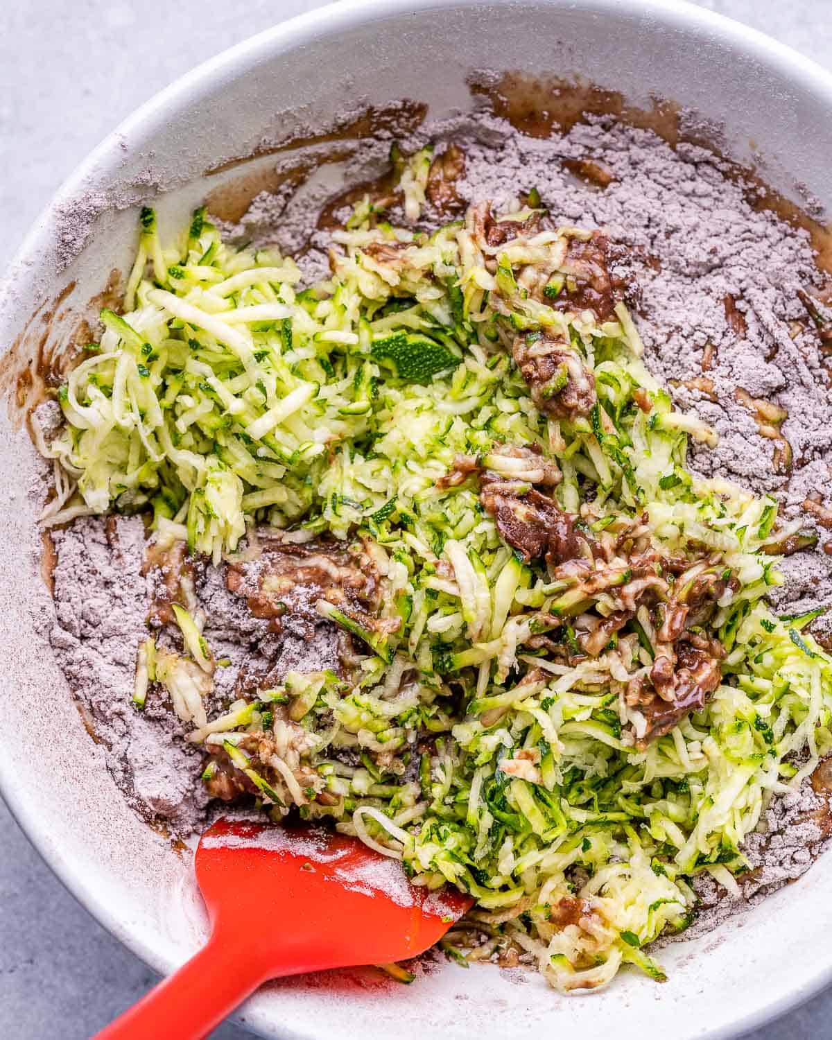 zucchini bread batter being mixed with red spatula