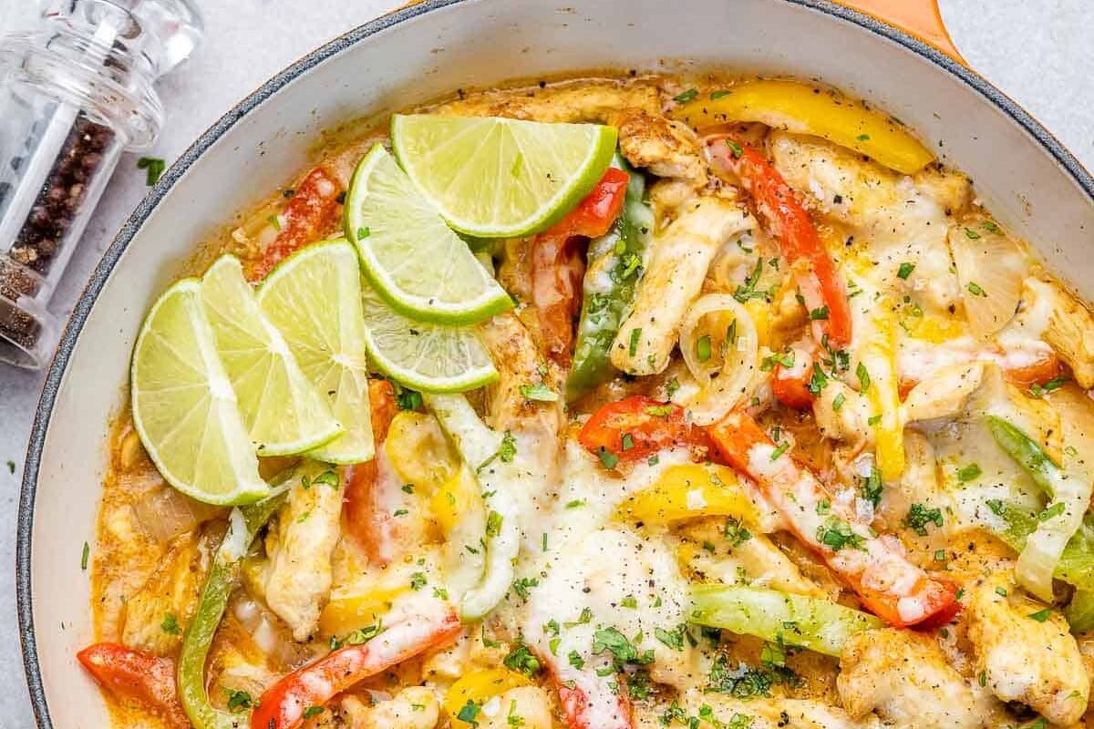 orange skillet with chicken fajita in it, topped with lime wedges