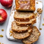 half of an apple bread sliced on a white cutting board.