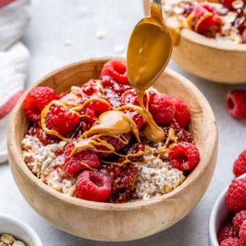 side shot of overnight oats in a brown wooden bowl topped with peanut butter drizzle and raspberries