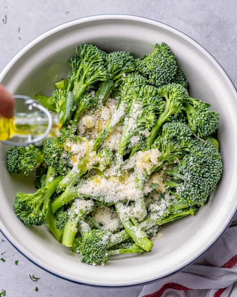 ingredients being added over raw broccolini in a bowl before roasting