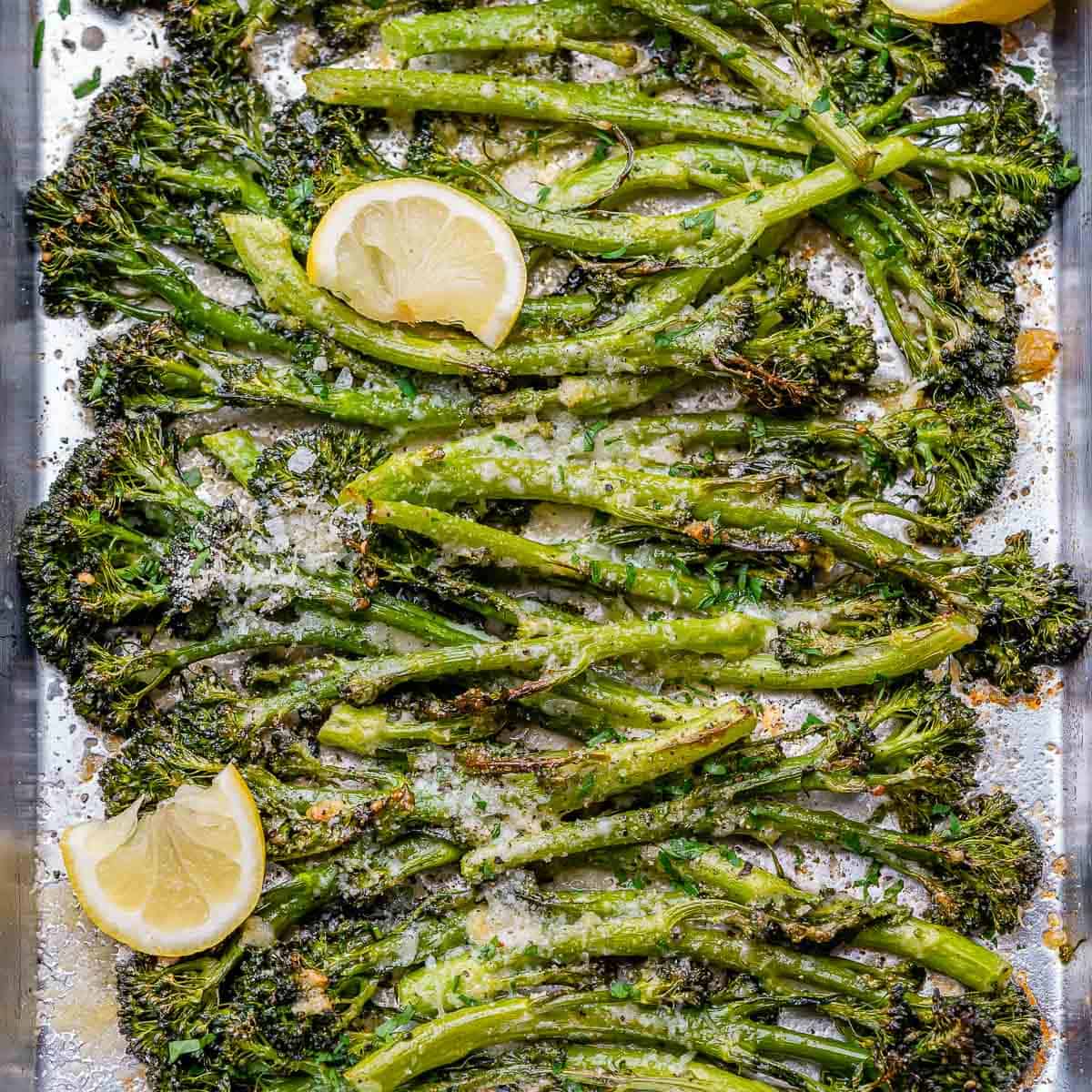 top view of roasted broccolini on a pan with lemon wedges