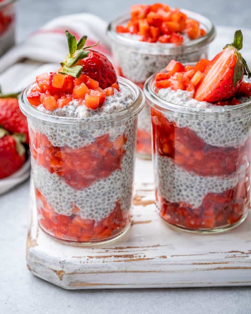 3 jars of chia pudding on a white wood platter