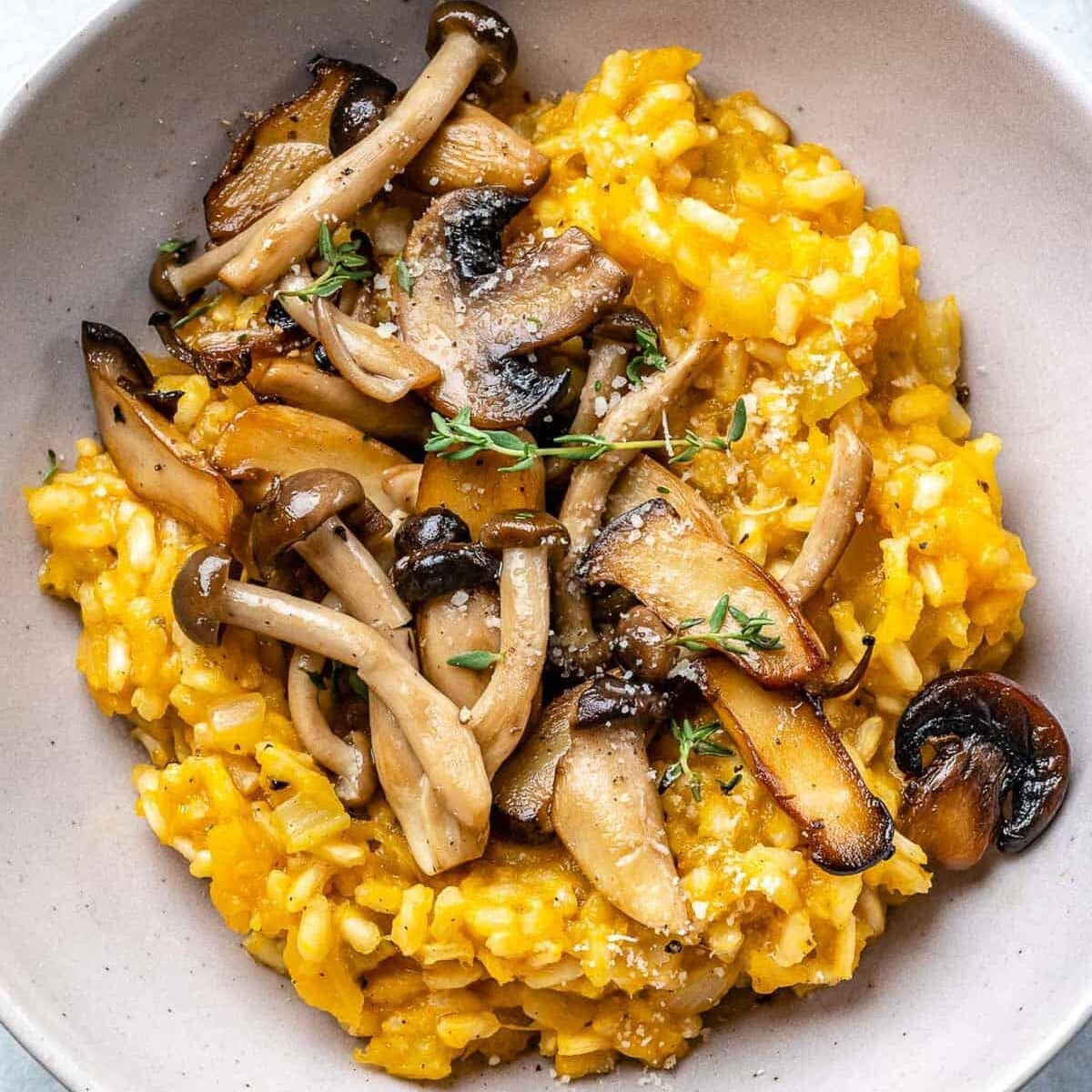 a bowl filled with orange colored risotto topped with sauteed mushrooms.