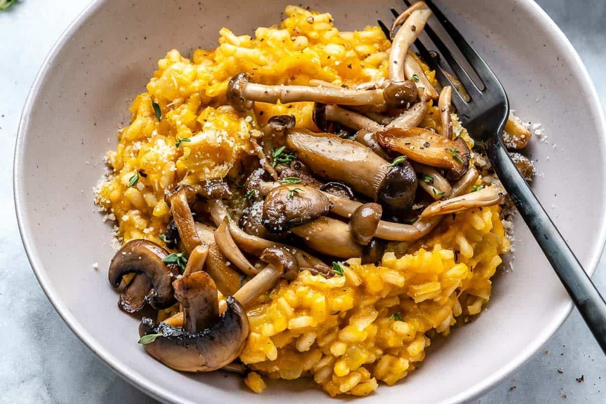 butternut squash risotto in a bowl topped with sauteed mushrooms.