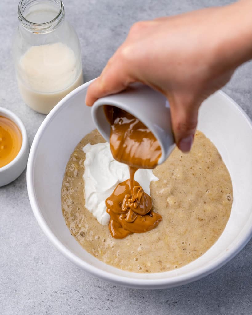 nut butter being poured over a bowl or mashed banana and yogurt