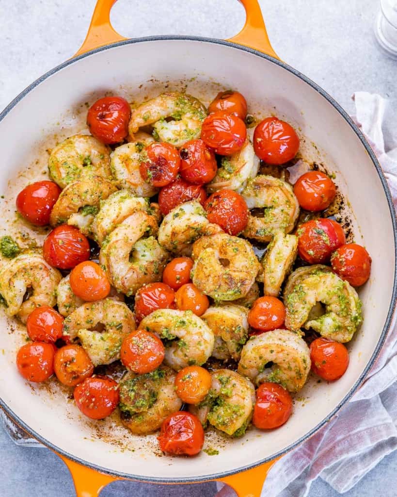 top view pesto shrimp in a orange pan with sauteed cherry tomatoes