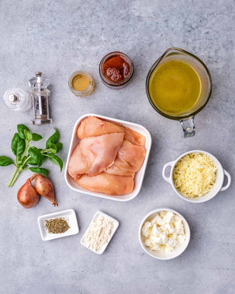 ingredients to make the cheese and tomato stuffed chicken breast. The image has raw chicken breast, cheese, herbs, stock, basil, and onions.