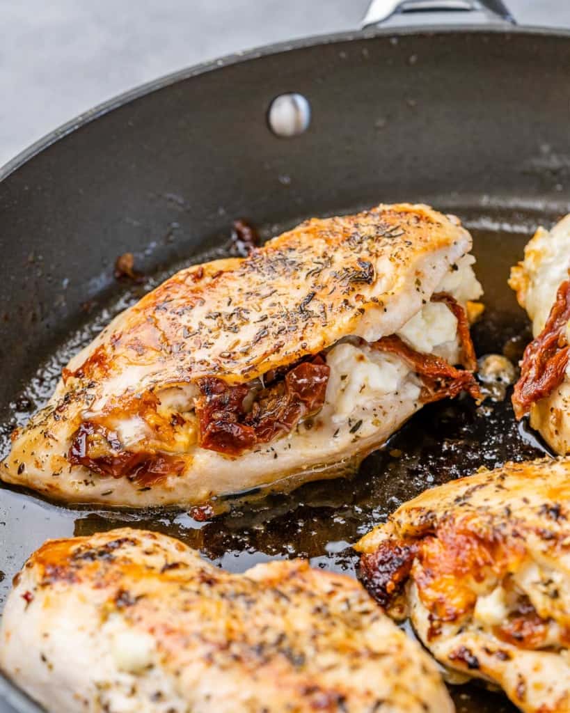 close up side shot of stuffed chicken breasts with tomatoes and cheese in a black skillet