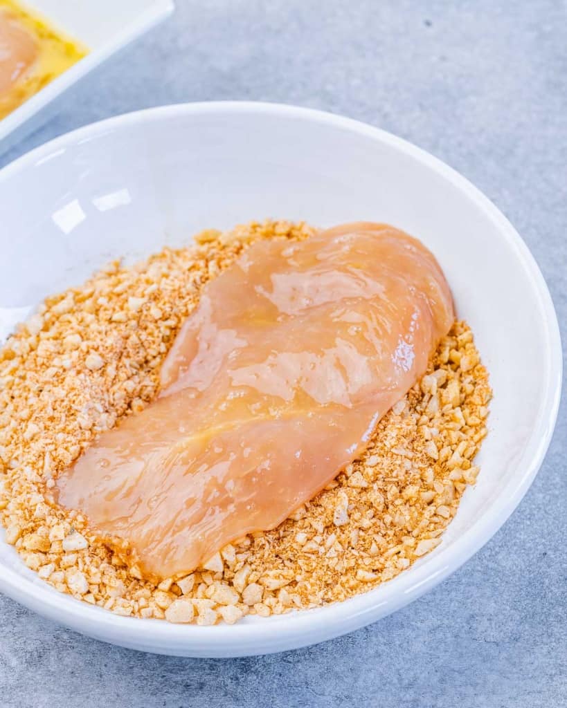 chicken breast being added over the seasoned almond crumbs to be coated 