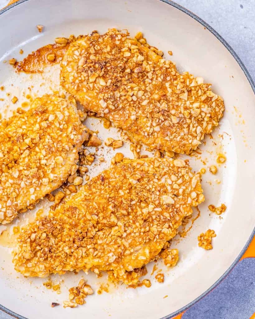 3 cooked almond crusted chicken breast in a skillet 