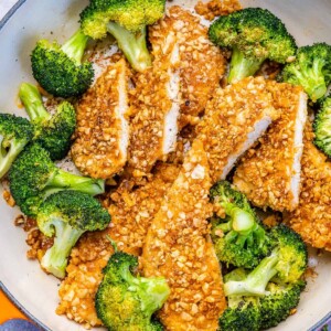 tope close up view of sliced almond crusted chicken breast with steamed broccoli in a skillet