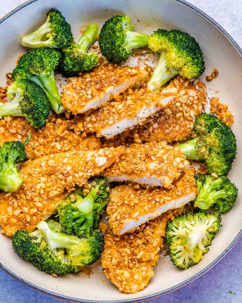 top view sliced almond crusted crispy chicken breast with a side of broccoli in a pan