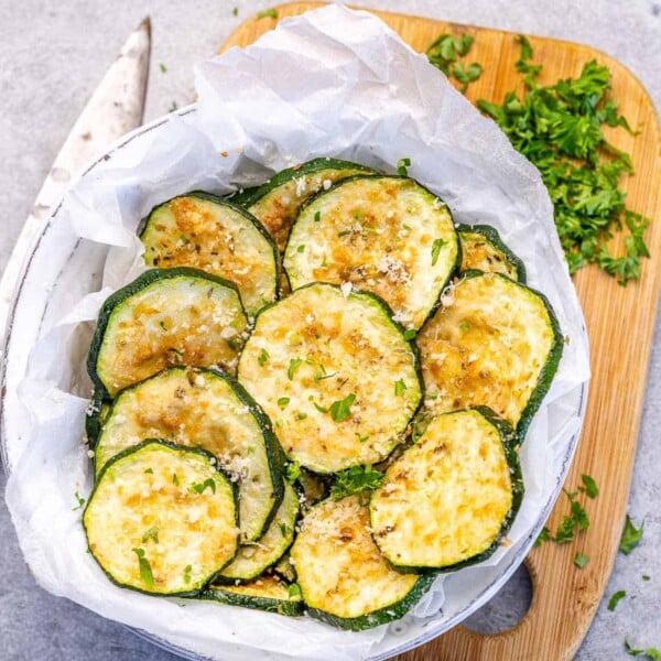 baked sliced zucchini in a bowl on a brown cutting board