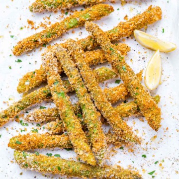 close up image of crispy asparagus on a pan with 2 lemon wedges to garnish