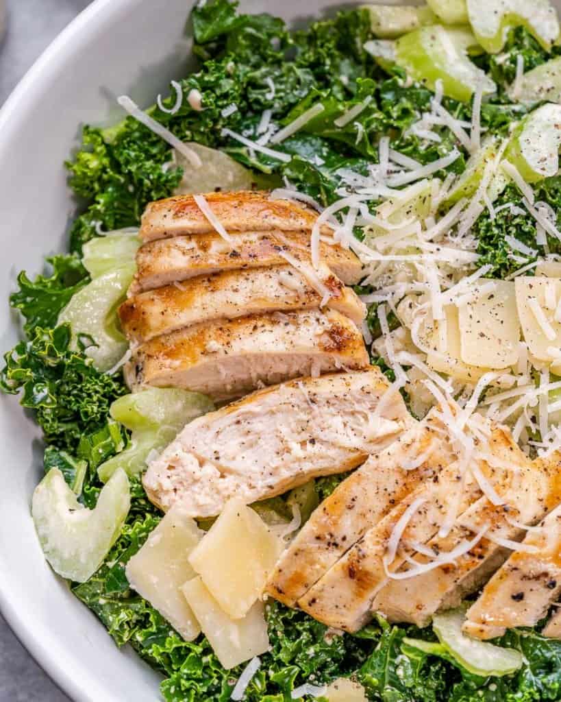 close up view of sliced chicken breast over kale salad topped with parmesan cheese