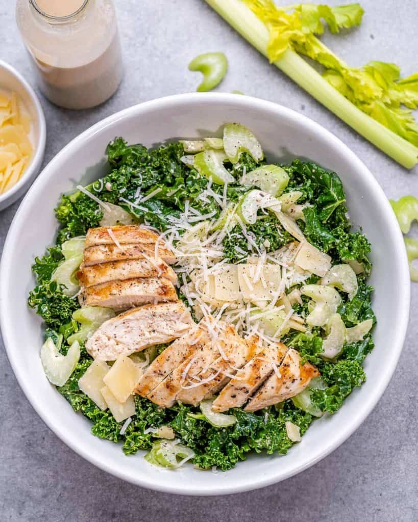 top view kale salad with sliced chicken breast in a white bowl with a side of dressing