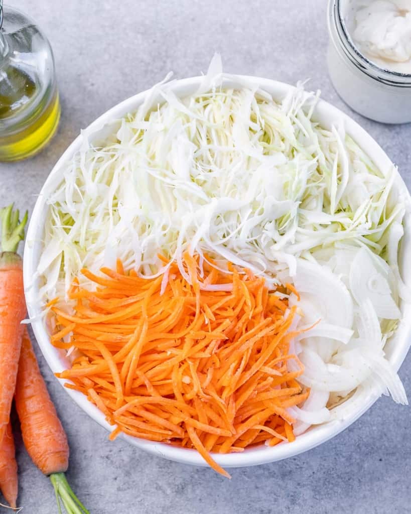 shredded carrots, shredded cabbage and sliced onions in a white bowl