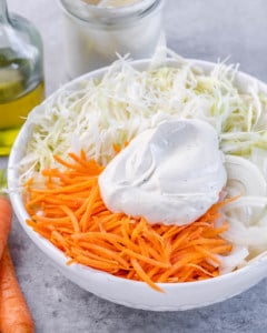 yogurt dressing dollop over the shredded carrots and cabbage in a white bowl before tossing together