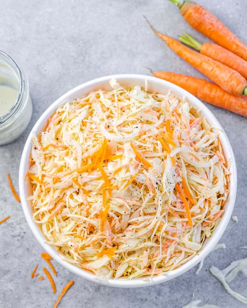 tope view of coleslaw salad in a white bowl with a side of fresh carrots next to the bowl on top right
