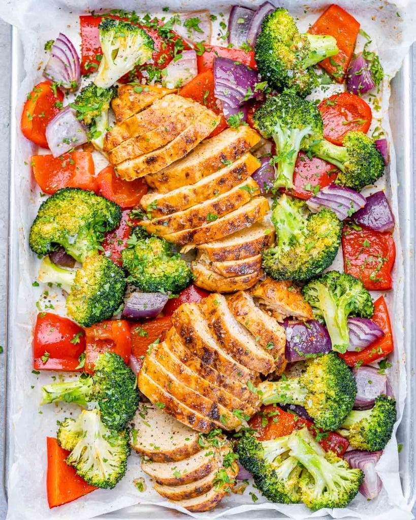 top view sliced baked chicken breast with roasted veggies on a sheet pan