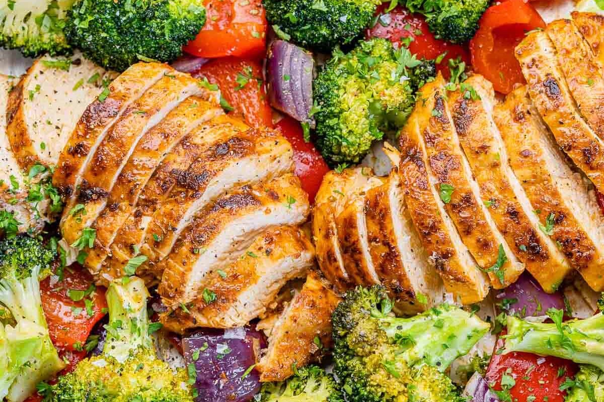 sliced baked chicken breast with roasted veggies on a pan