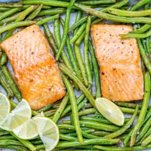top view two salmon filets baked on a sheet pan with green beans and sliced lime garnishes