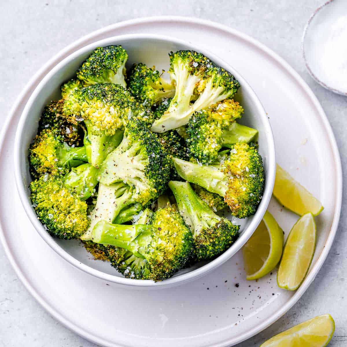 top view air fried broccoli in a white bowl over a white plate