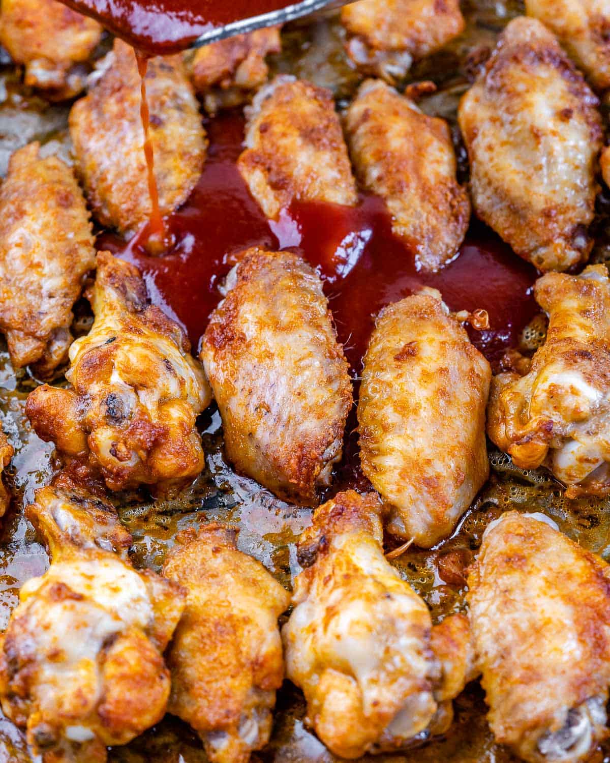 drizzling honey garlic sauce over baked crispy chicken wings 