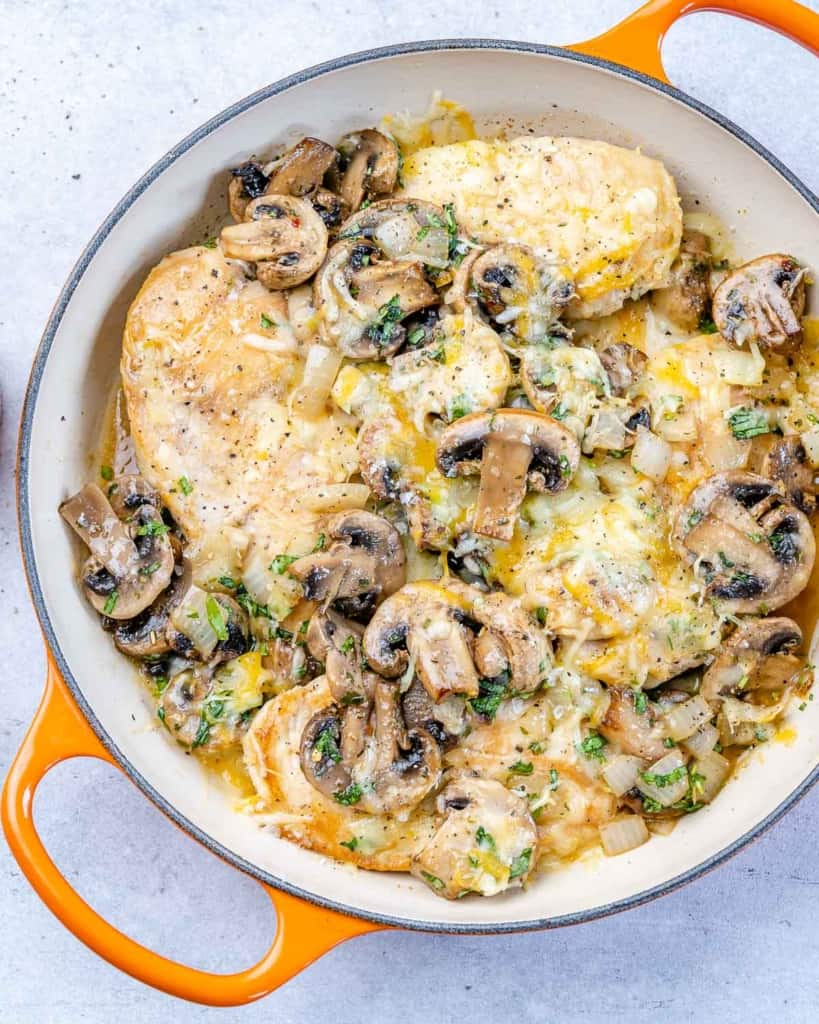 top view of cheesy chicken with mushrooms in orange skillet 