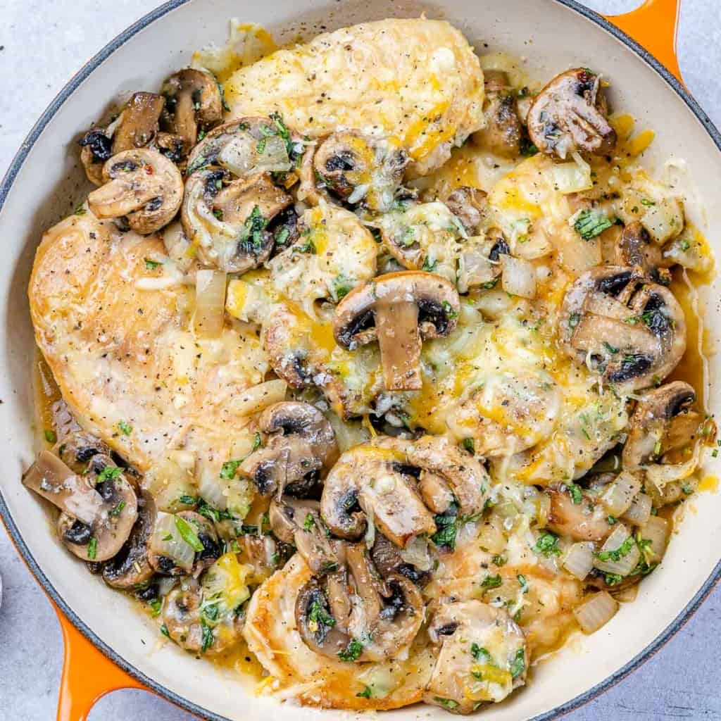 tope view of chicken breast satuteed with mushroom and topped with cheese over an orange skillet