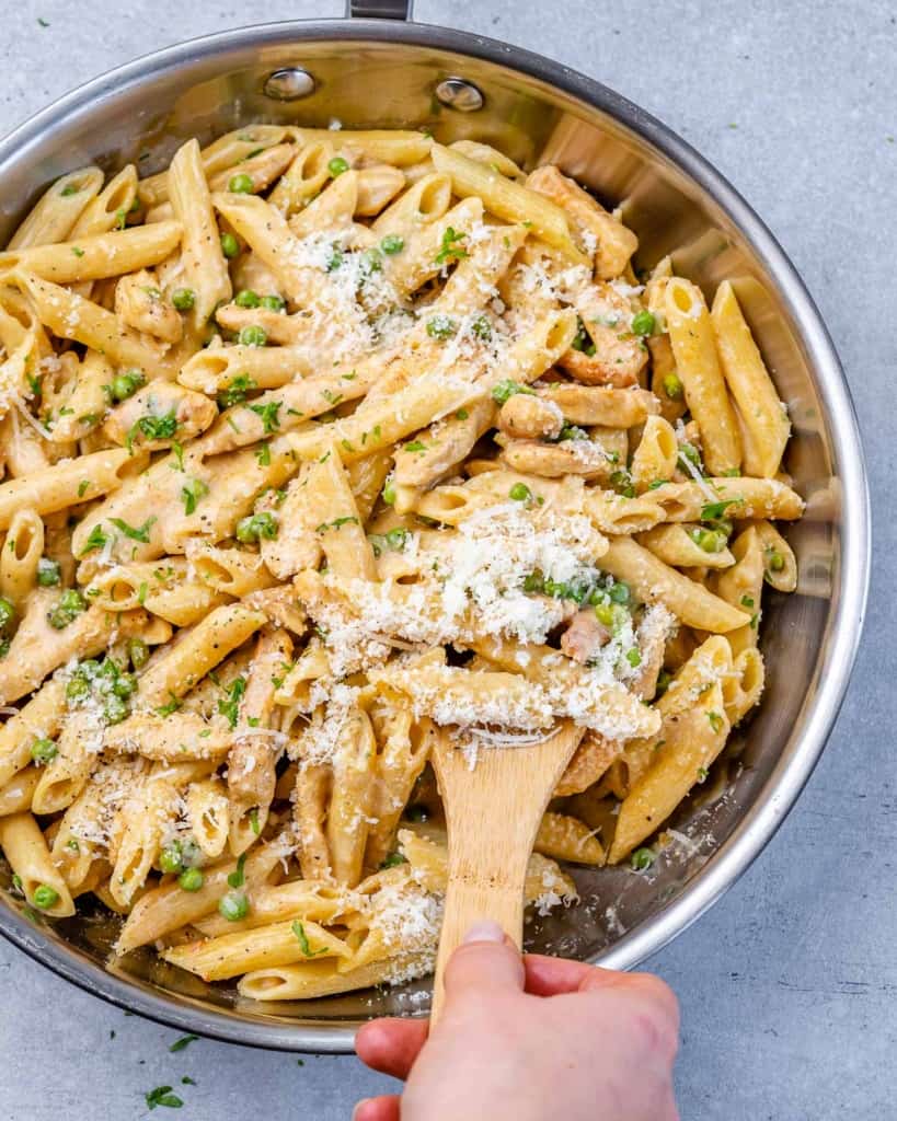 Hand serving Chicken Carbonara from a stainless steel pan with a wooden spoon.