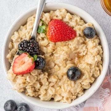 top view image of a white bowl that has cooked oatmeal topped with berries with a spoon in it