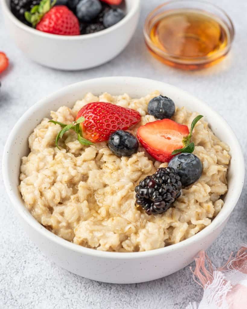 side shot of oatmeal breakfast bowl topped with berries with side of maple syrup