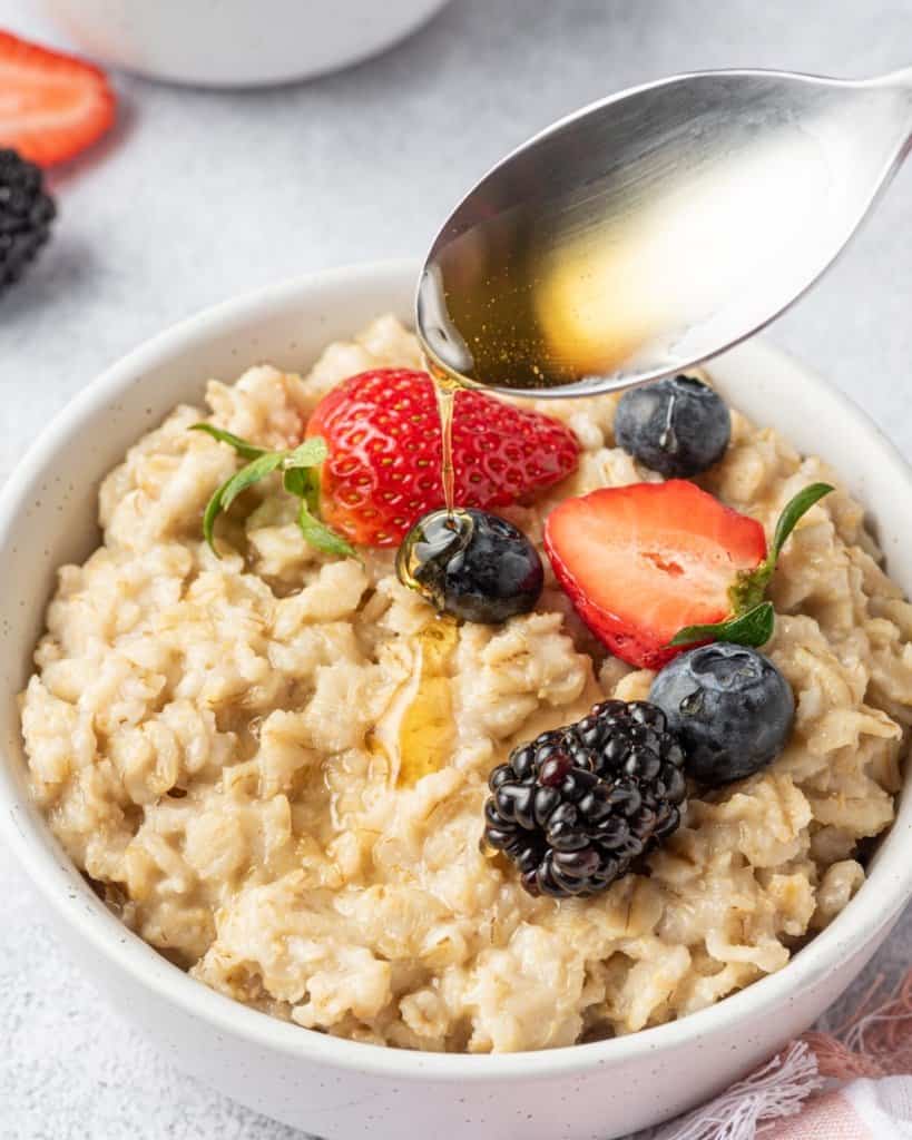 maple syrup being added over a bowl of oatmeal topped with berries 