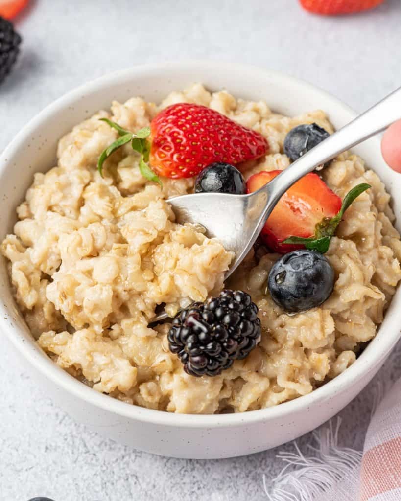 side shot of an oatmeal bowl with a spoon in it, topped with berries and maple syrup